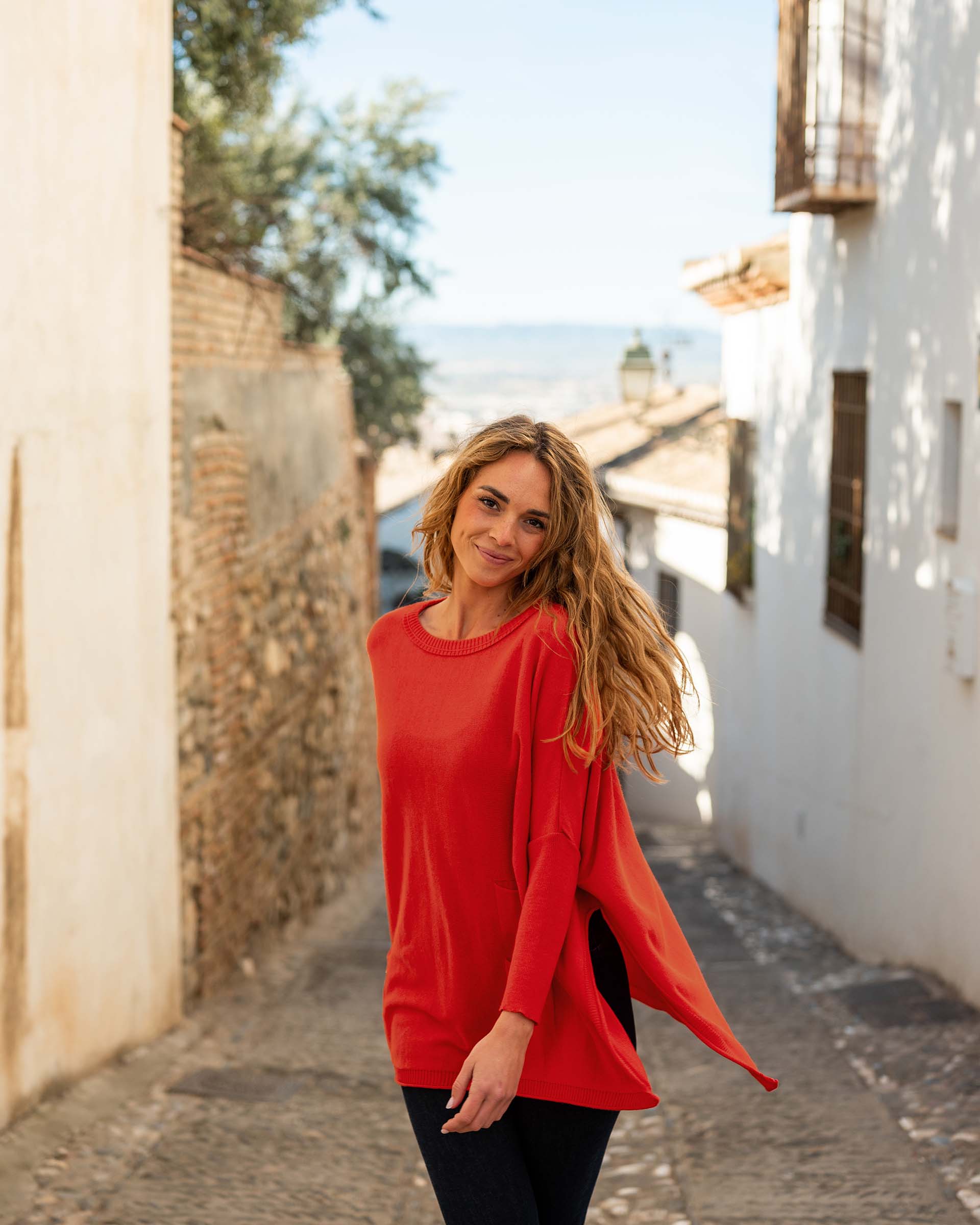 female wearing red sweater with dark jeans spinning in the streets of the country side of spain