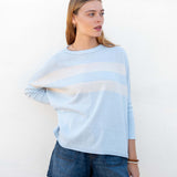 Woman wearing a light blue sweater with a white stripe and denim shorts against a white background