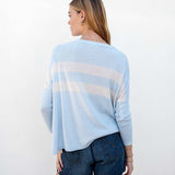 Woman wearing a light blue sweater with white stripes and denim shorts on a white background