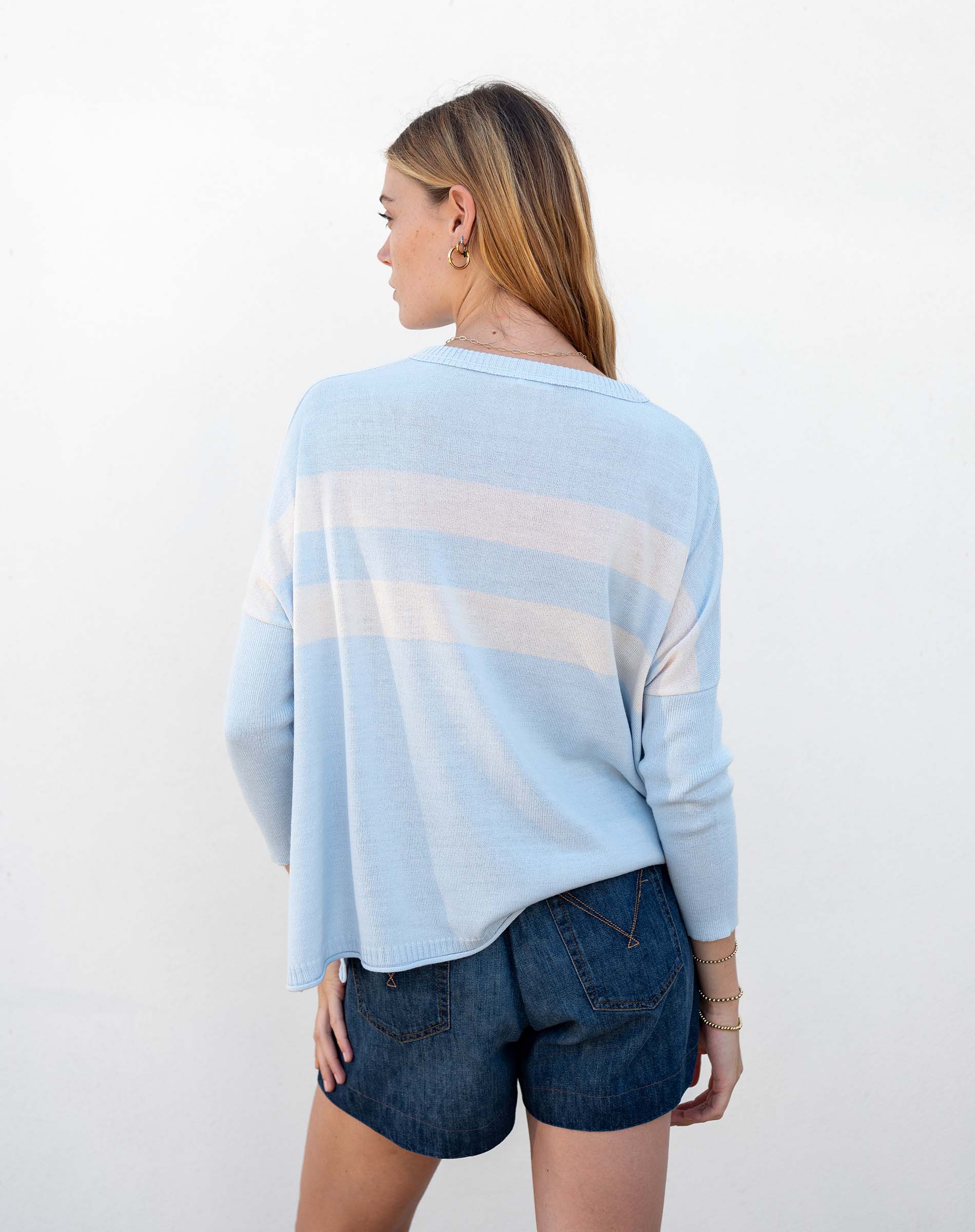 Woman wearing a light blue sweater with white stripes and denim shorts on a white background