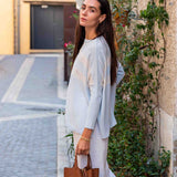 Woman in light blue top and white pants holding a brown bag on a street.