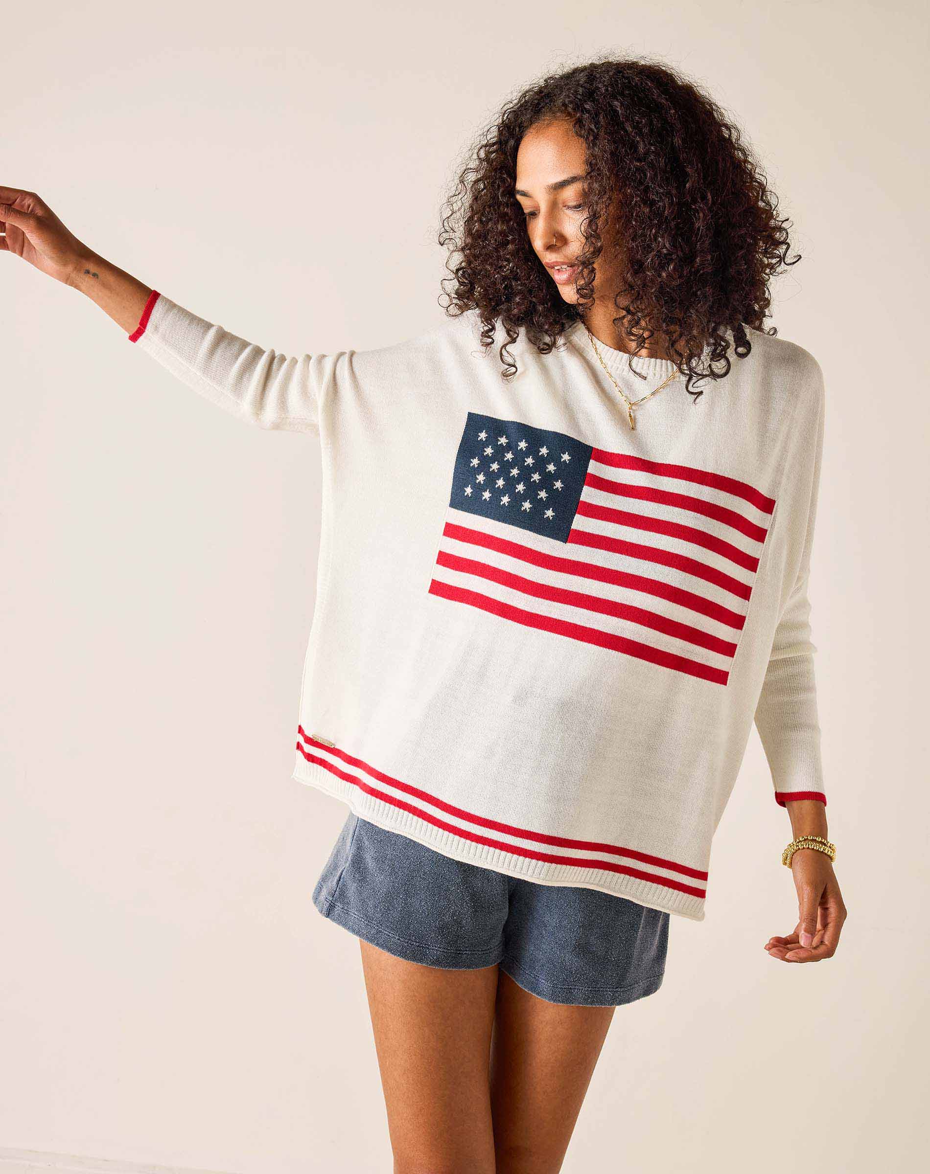 Woman wearing a white sweater with an American flag design on a plain background