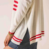 White sweater with red stripes worn by a person on a light pink background