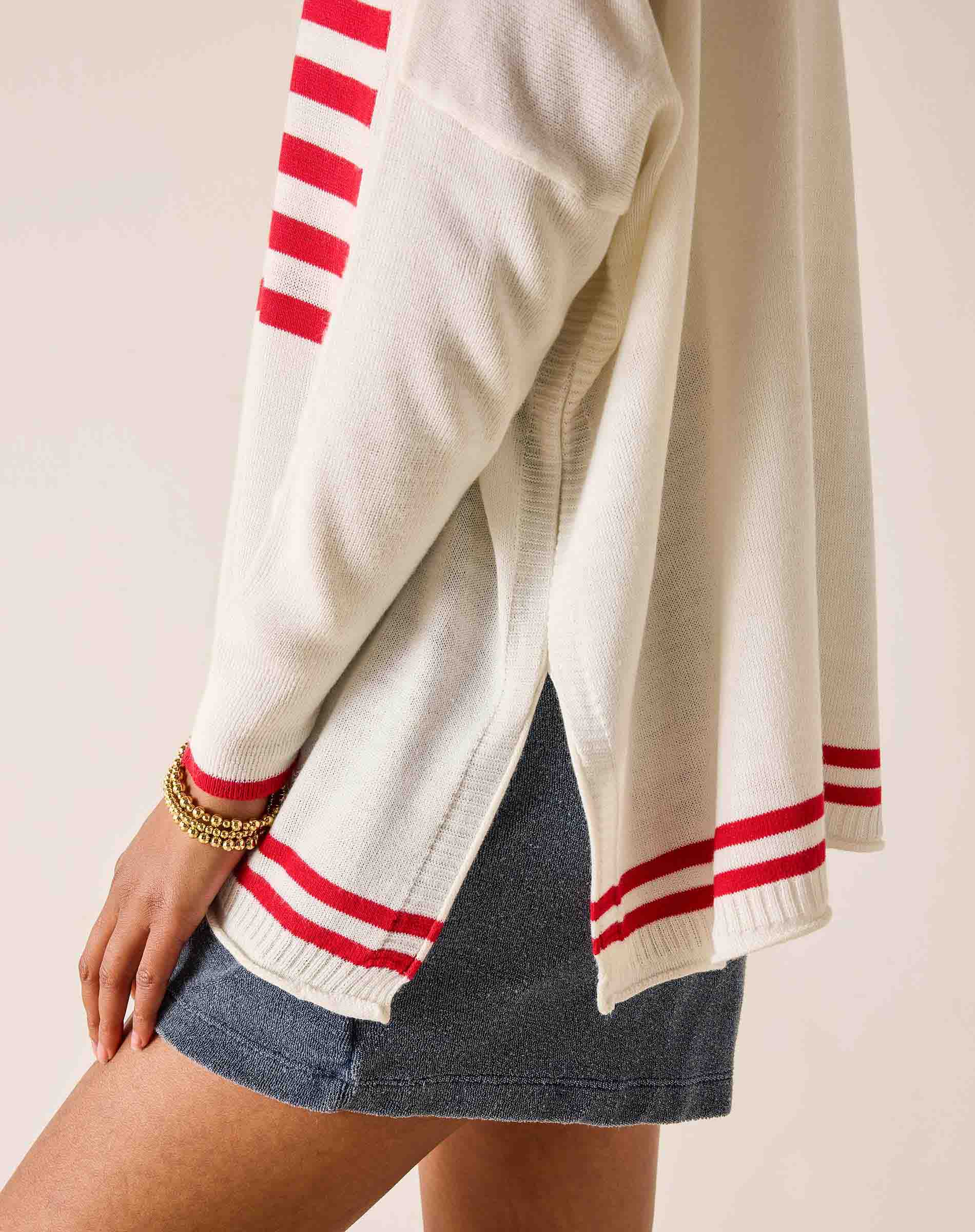 White sweater with red stripes worn by a person on a light pink background