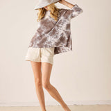 Woman wearing a tie-dye shirt and shorts with a hat on a plain background