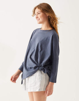 female wearing dark blue long sleeve tee shirt tied at the hip and striped shorts on a white wall