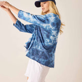 Person wearing a blue tie-dye shirt and white shorts with a plain background