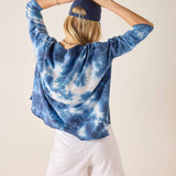 Person wearing a blue tie-dye hoodie and white shorts with a plain background