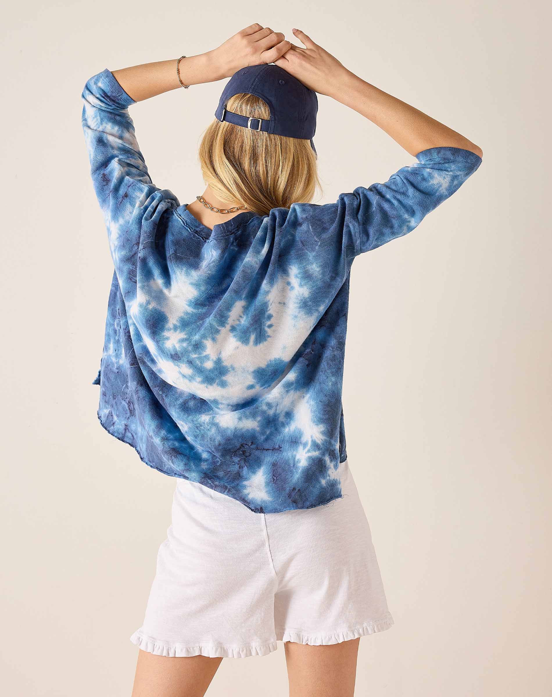 Person wearing a blue tie-dye hoodie and white shorts with a plain background