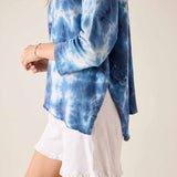 Person wearing a blue tie-dye long-sleeve top with a white skirt on a beige background