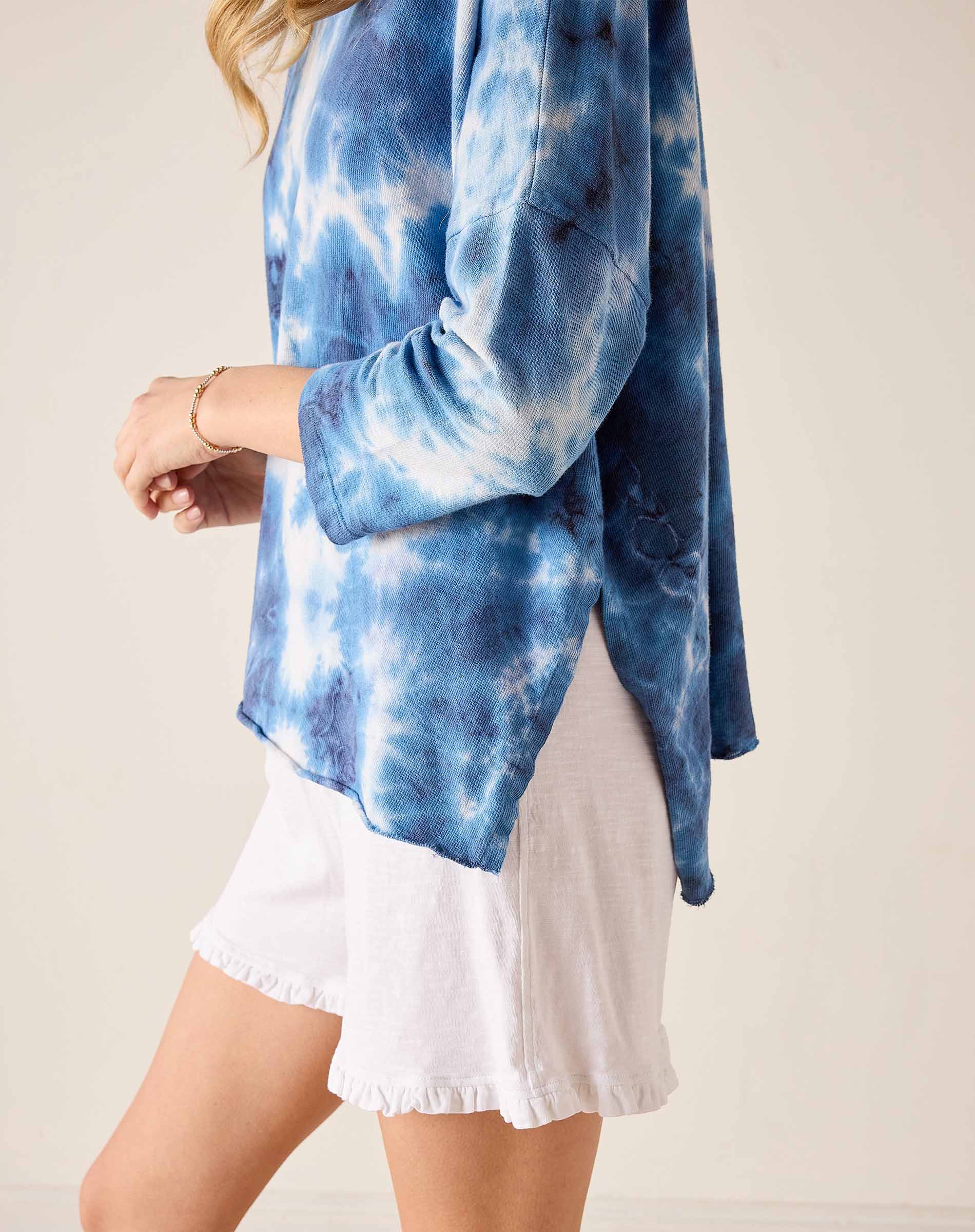 Person wearing a blue tie-dye long-sleeve top with a white skirt on a beige background