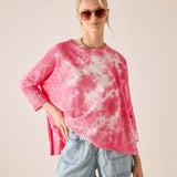 Person wearing a pink tie-dye shirt and denim shorts on a beige background