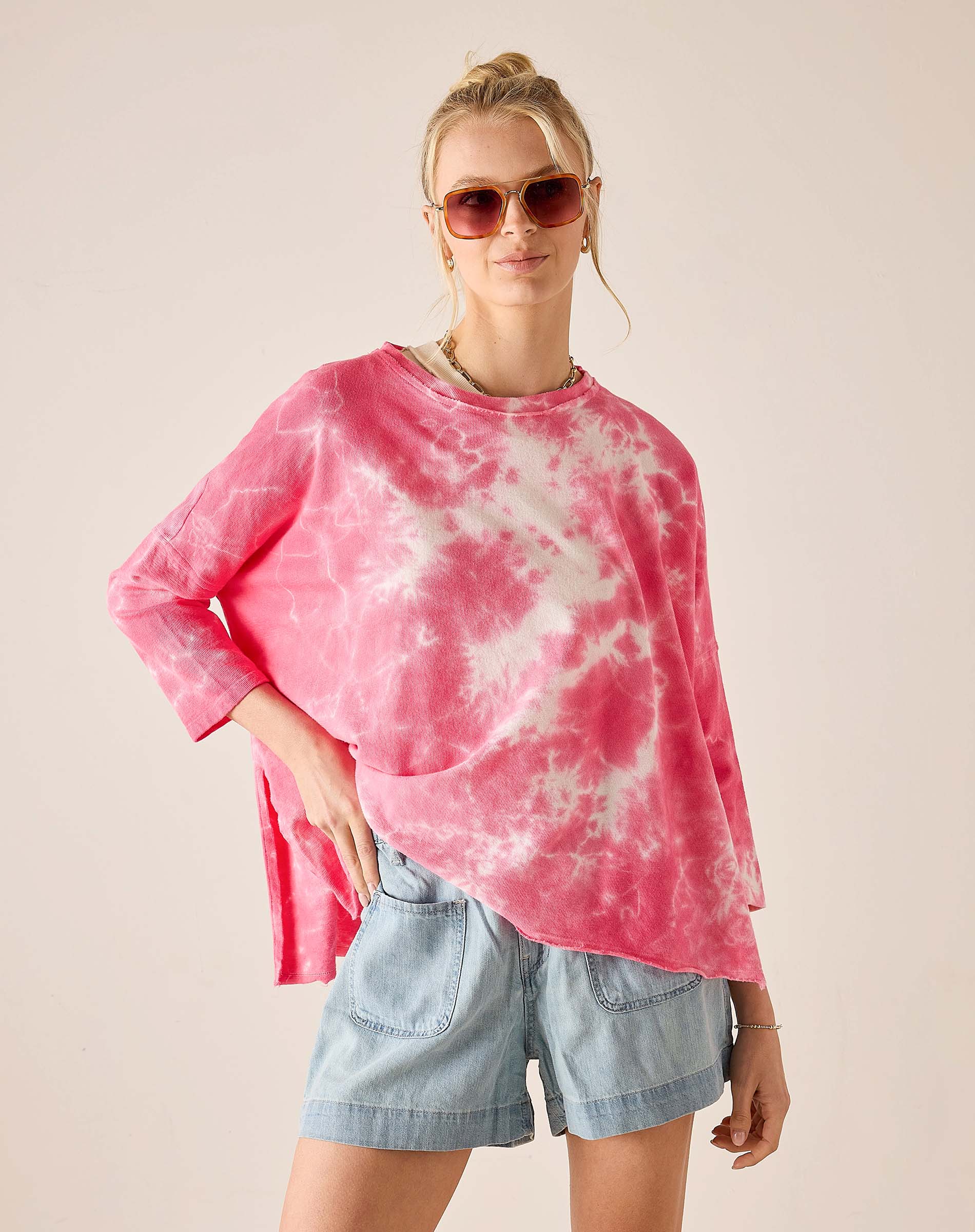 Person wearing a pink tie-dye shirt and denim shorts on a beige background