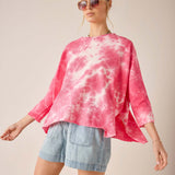 Woman wearing a pink tie-dye shirt and denim shorts on a plain background