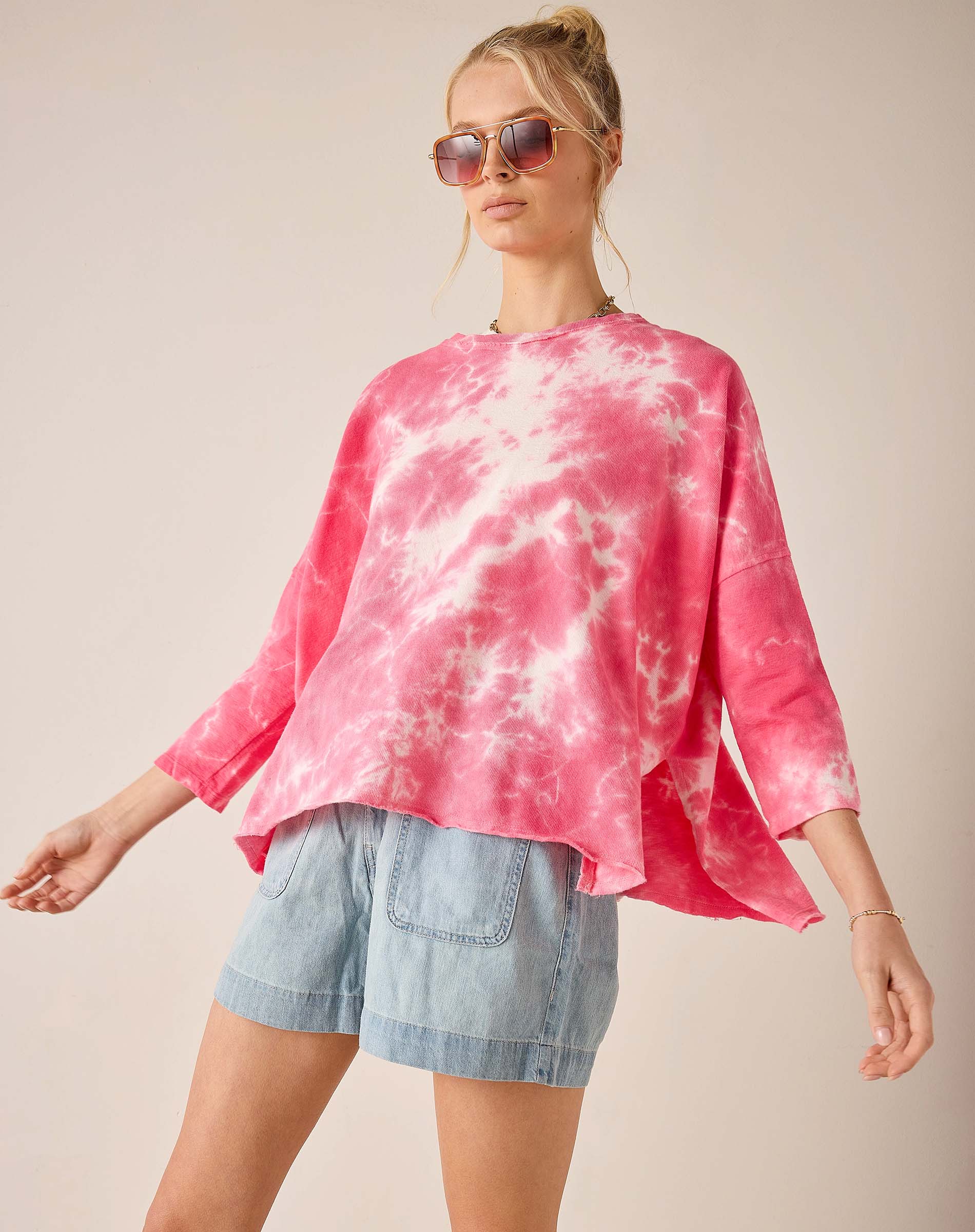 Woman wearing a pink tie-dye shirt and denim shorts on a plain background