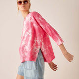 Person wearing a pink tie-dye shirt and denim shorts on a plain background