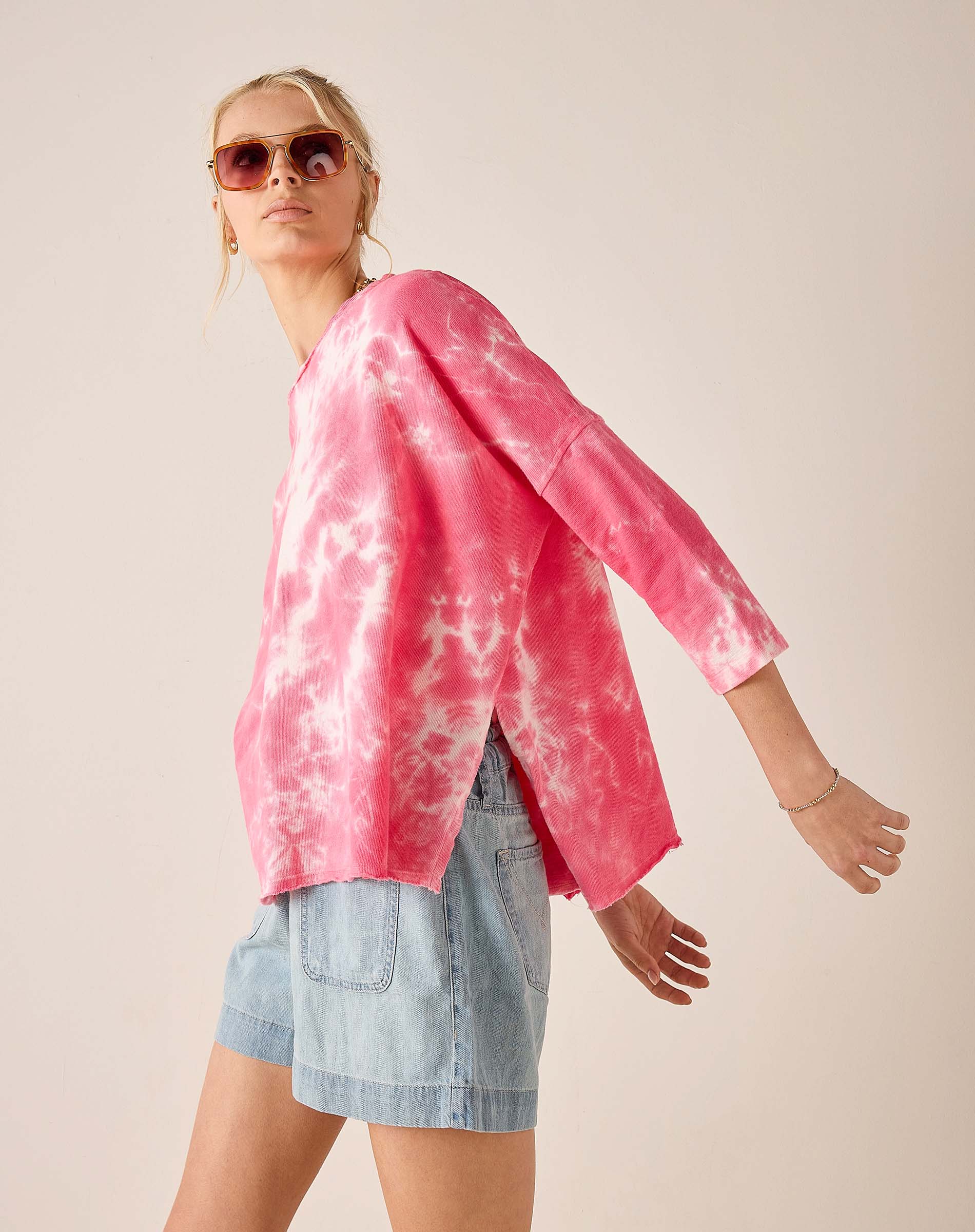 Person wearing a pink tie-dye shirt and denim shorts on a plain background