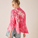 Person wearing a pink tie-dye shirt and denim shorts on a plain background