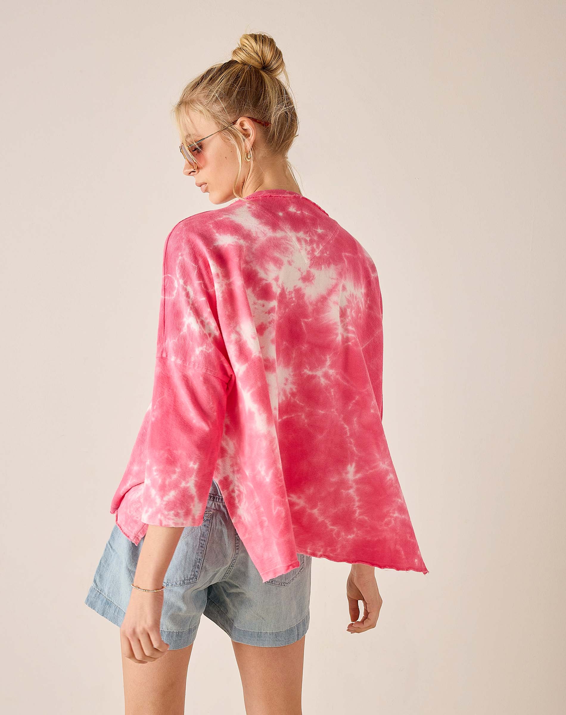 Person wearing a pink tie-dye shirt and denim shorts on a plain background