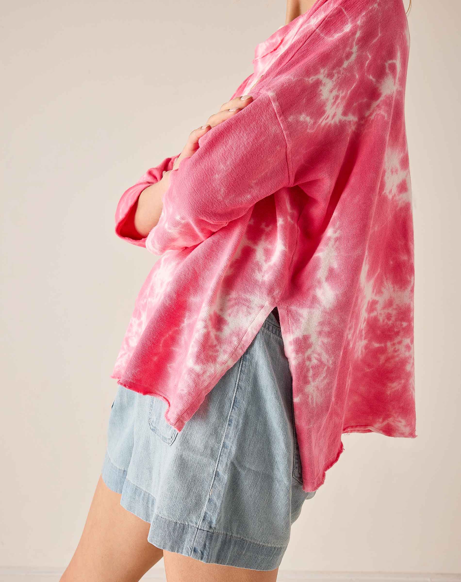 Person wearing a pink tie-dye shirt over a denim skirt on a plain background