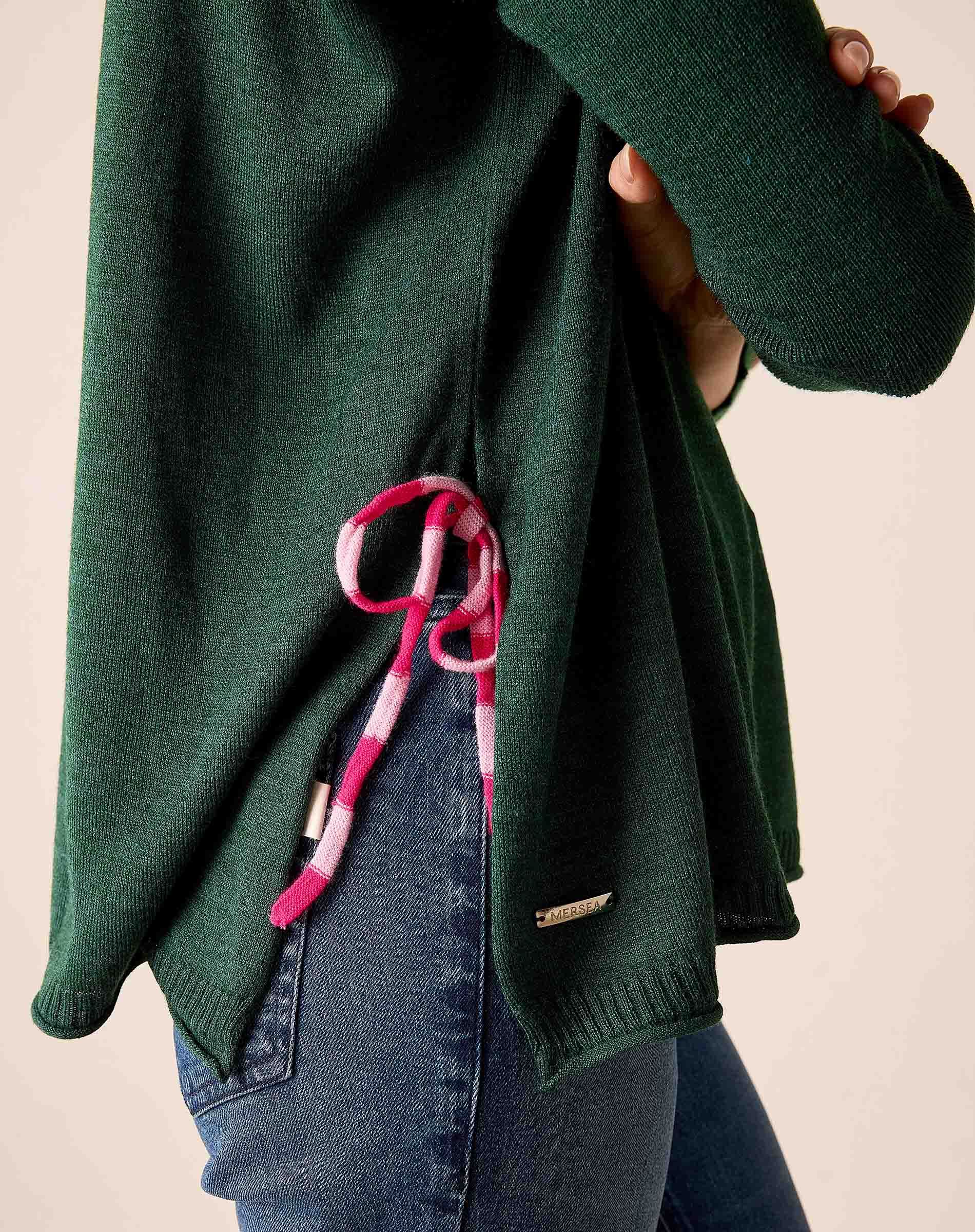 Forest green knit sweater with a pink and white striped tie-side detail and a small brand logo on the hem.