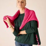 Berry pink textured knit travel wrap with ruffled edges and striped trim over a dark green ribbed knit tunic.