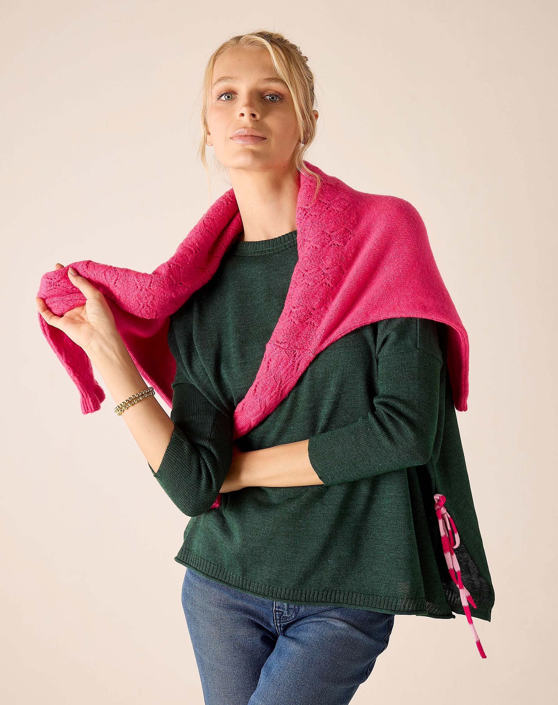 Berry pink textured knit travel wrap with ruffled edges and striped trim over a dark green ribbed knit tunic.