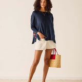 Woman wearing a navy sweater and white shorts, holding a red and white bag with a straw handle.
