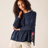 Woman wearing a navy sweater with a patterned scarf and beige shorts on a plain background