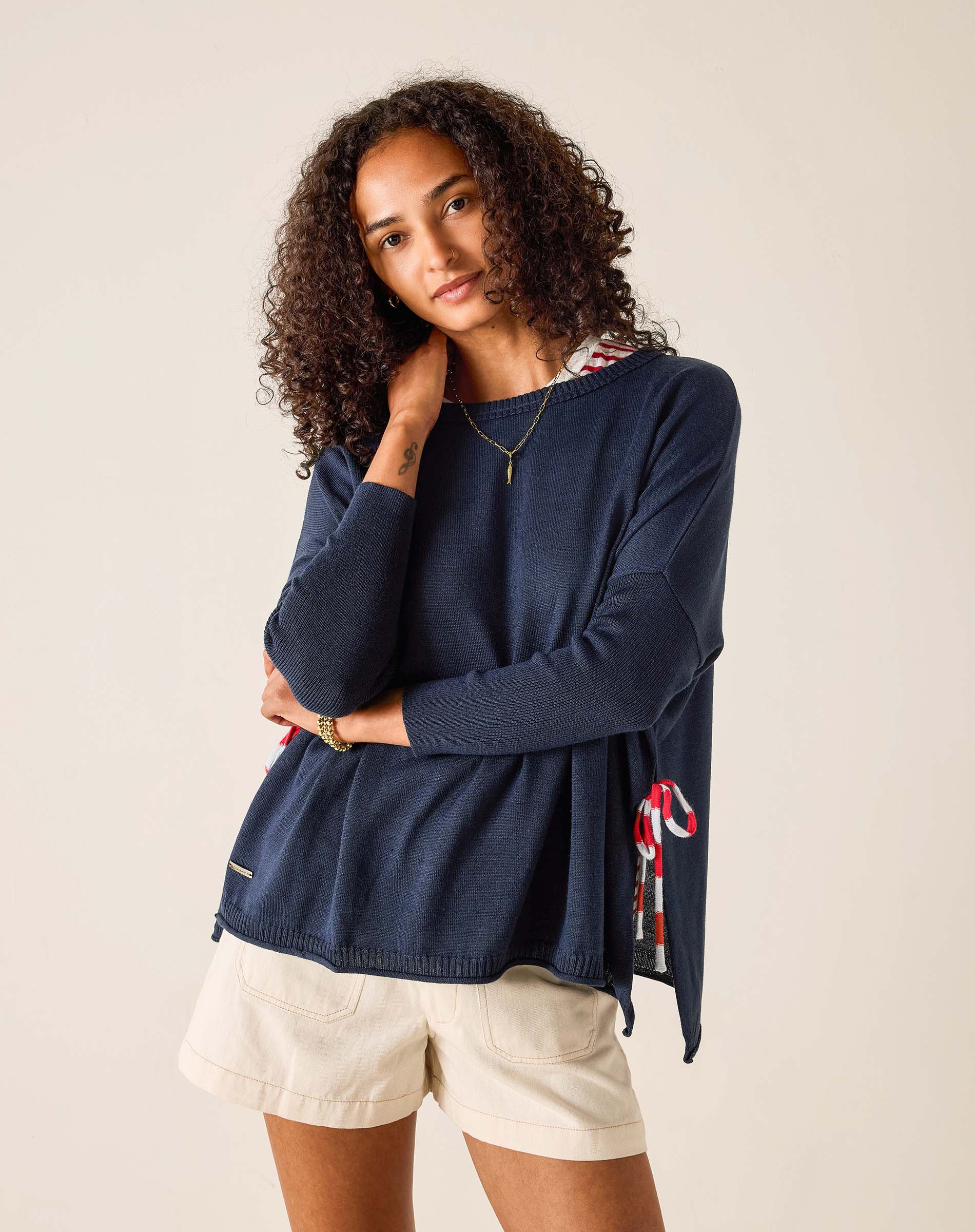 Woman wearing a navy sweater with a patterned scarf and beige shorts on a plain background