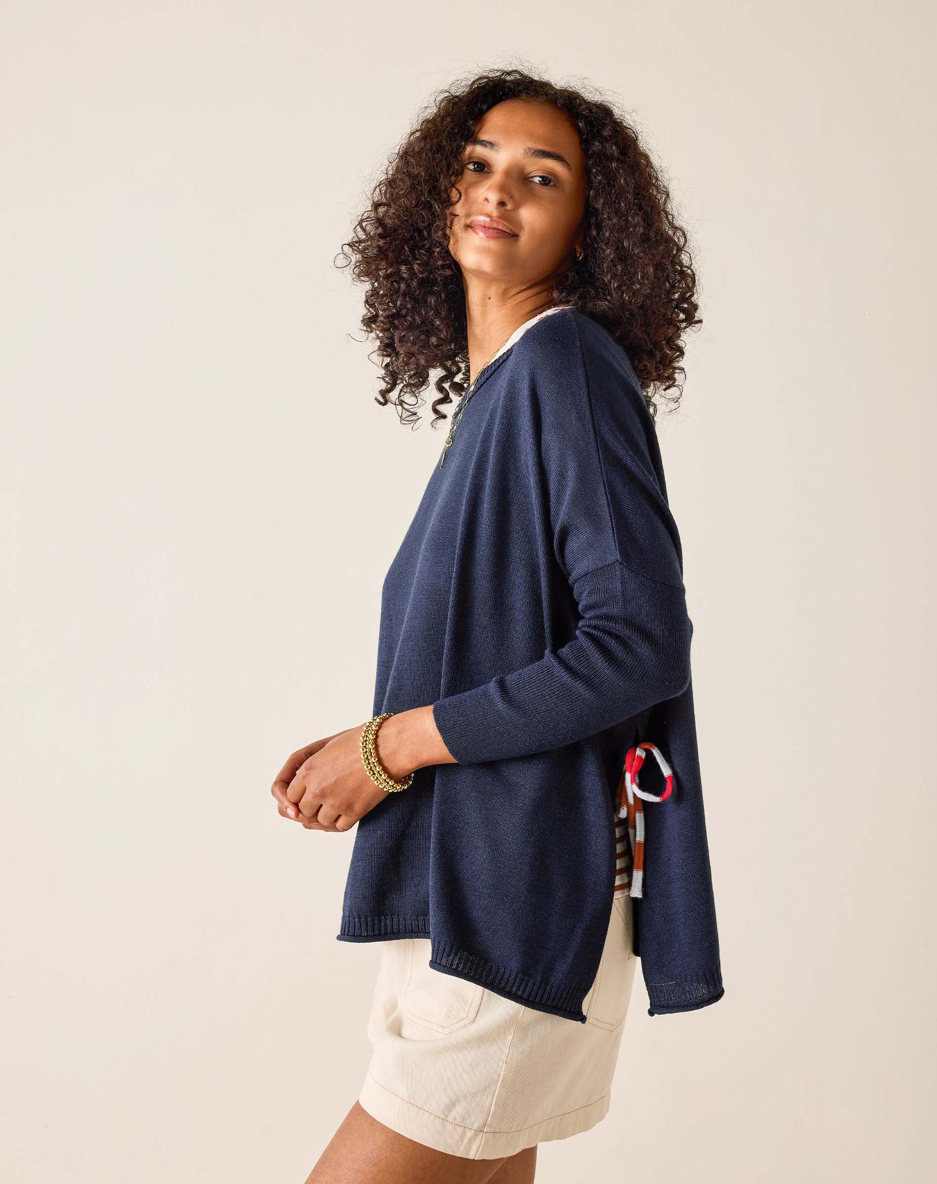 Woman wearing a navy cardigan over a white shirt with beige shorts on a plain background