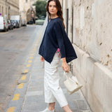 Woman in navy jacket and white pants standing on a city street.