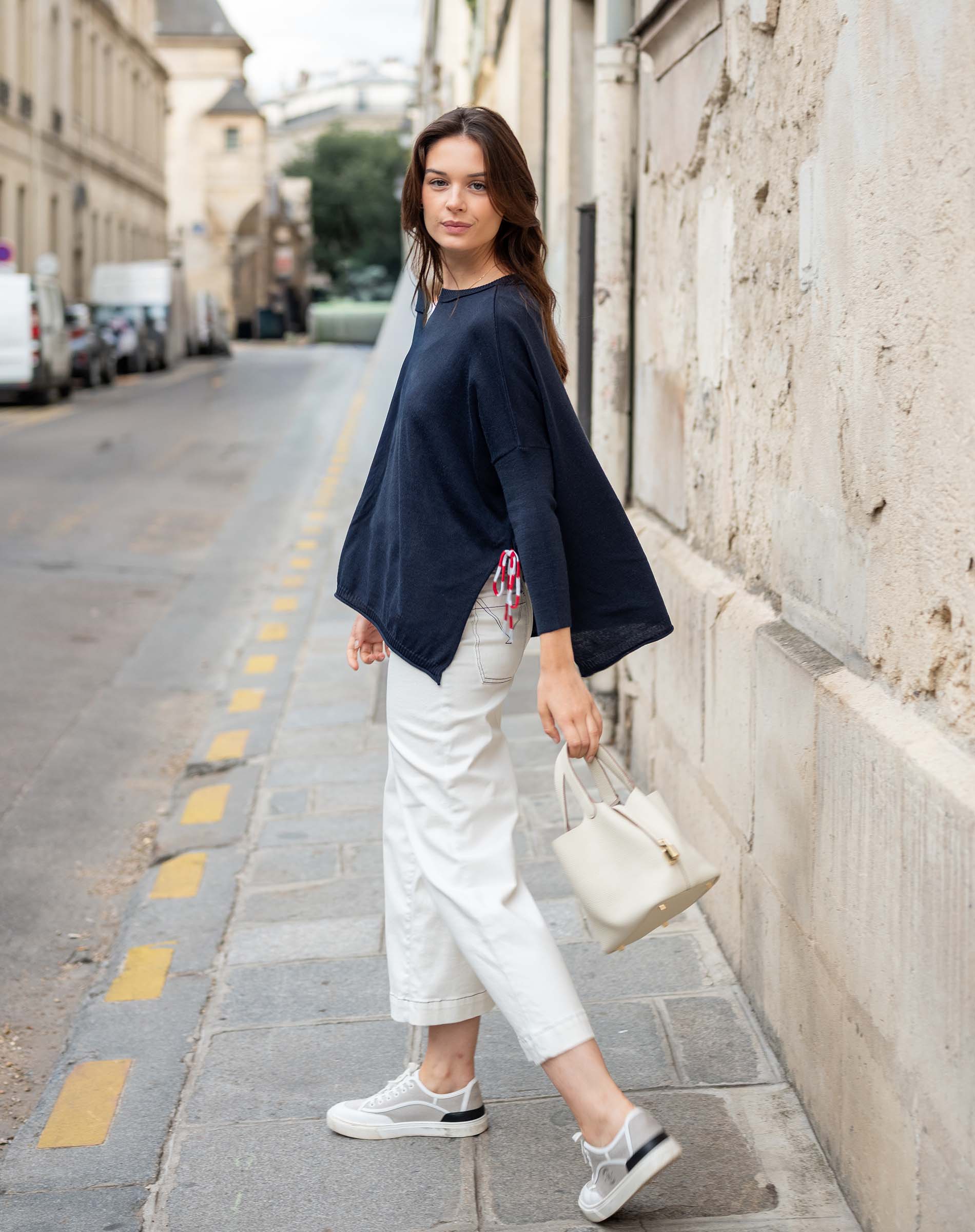 Woman in navy jacket and white pants standing on a city street.