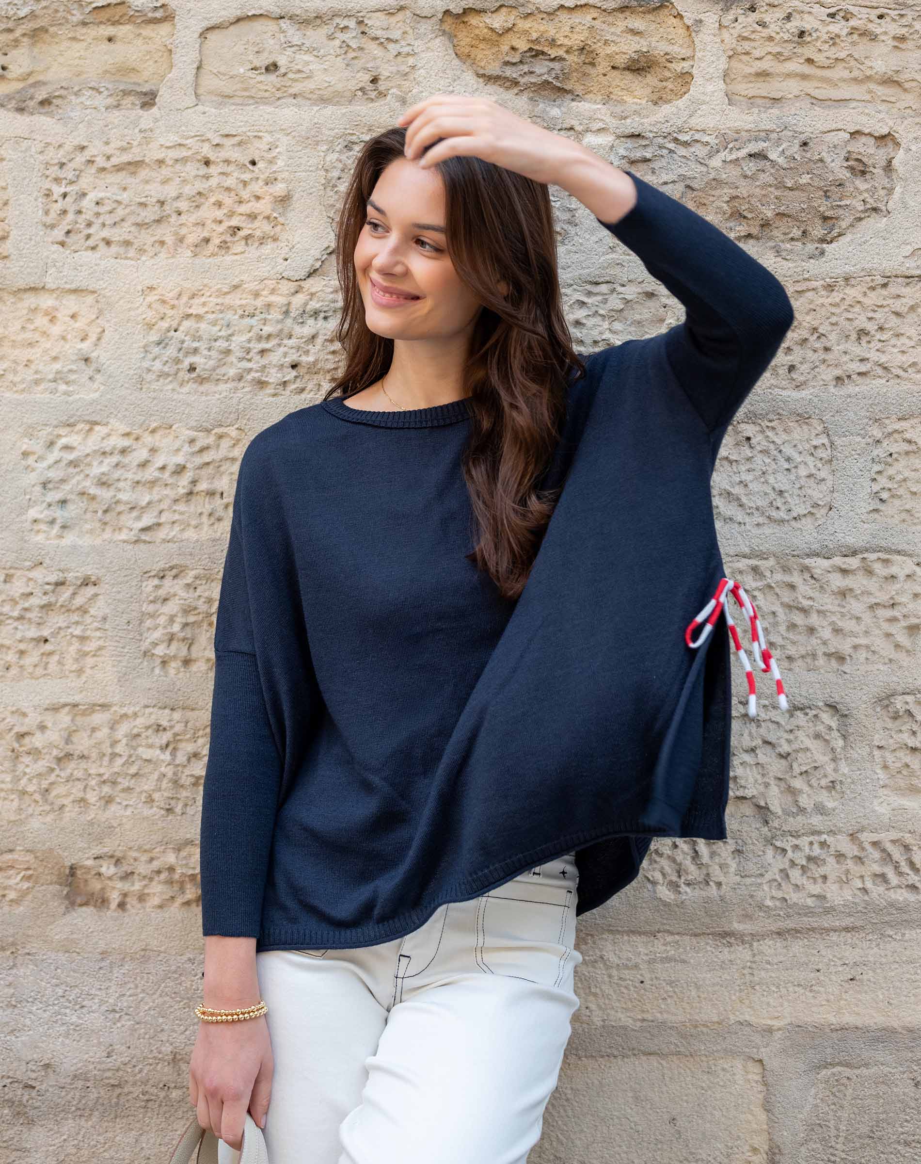 Woman wearing a navy blue sweater with a stone wall background