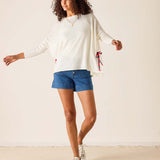 Woman wearing a white sweater, blue shorts, and white sneakers on a plain background