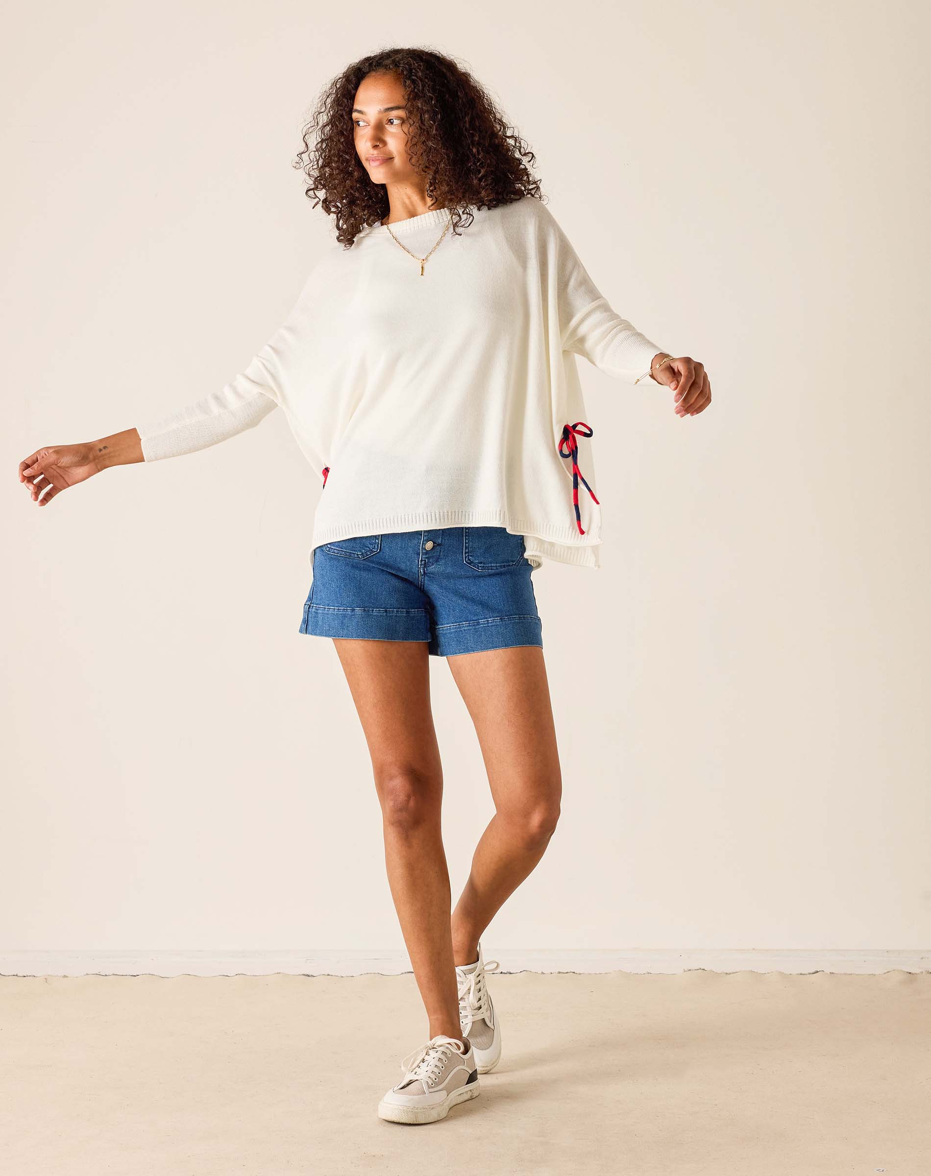 Woman wearing a white sweater, blue shorts, and white sneakers on a plain background