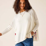 Woman wearing a white sweater with colorful accents and denim shorts on a beige background