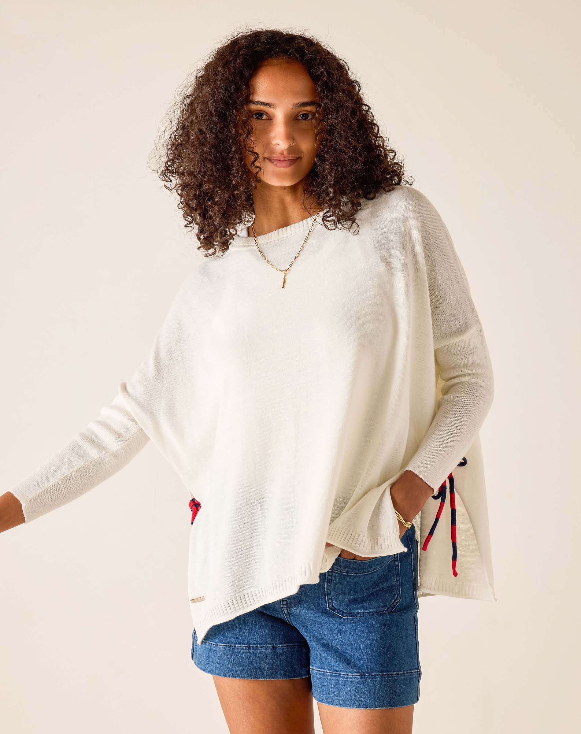 Woman wearing a white sweater with colorful accents and denim shorts on a beige background