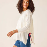 Woman wearing a white sweater and blue shorts with a red and black ribbon on a beige background