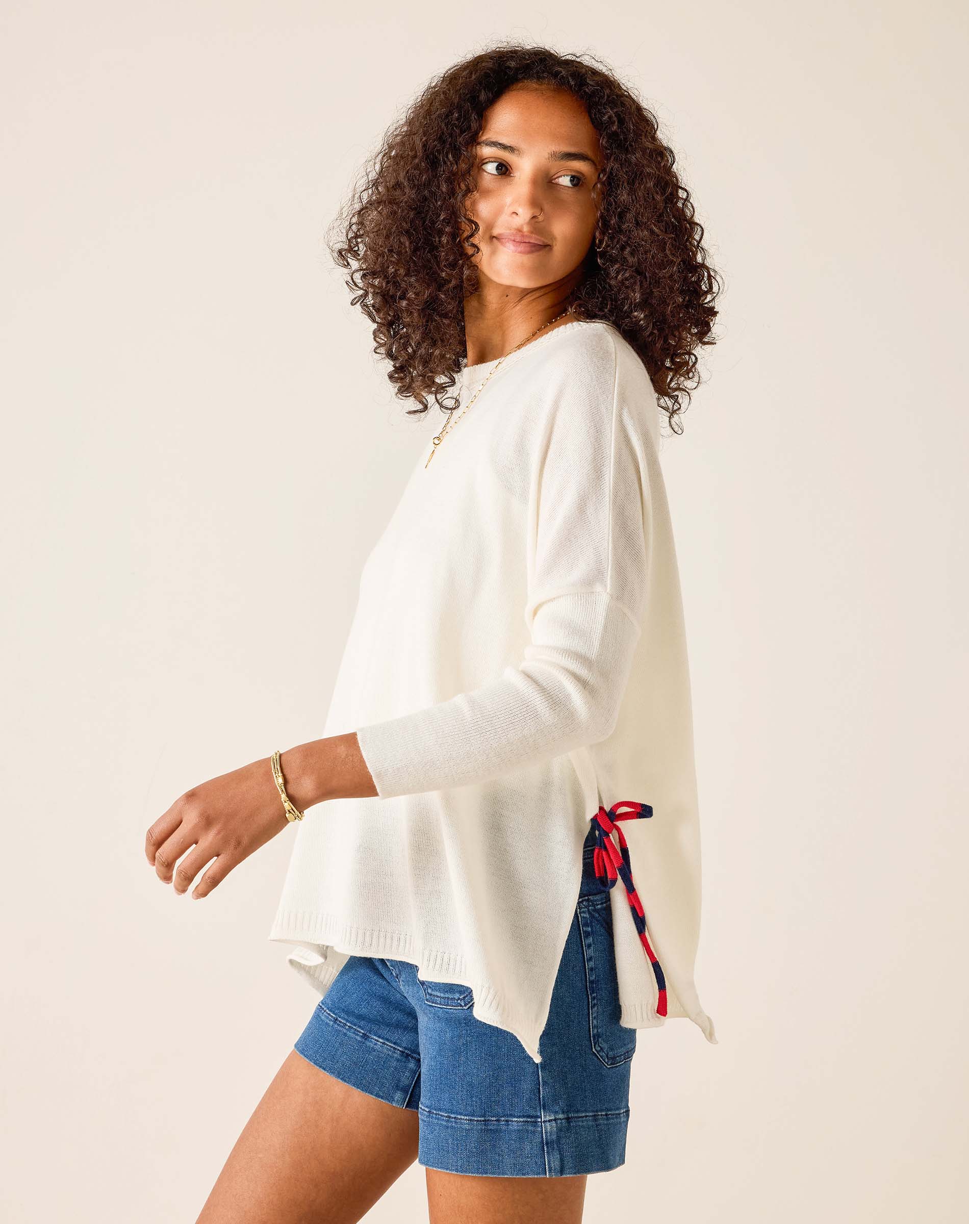 Woman wearing a white sweater and blue shorts with a red and black ribbon on a beige background