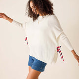 Woman wearing a white sweater with red and blue accents and denim shorts on a beige background