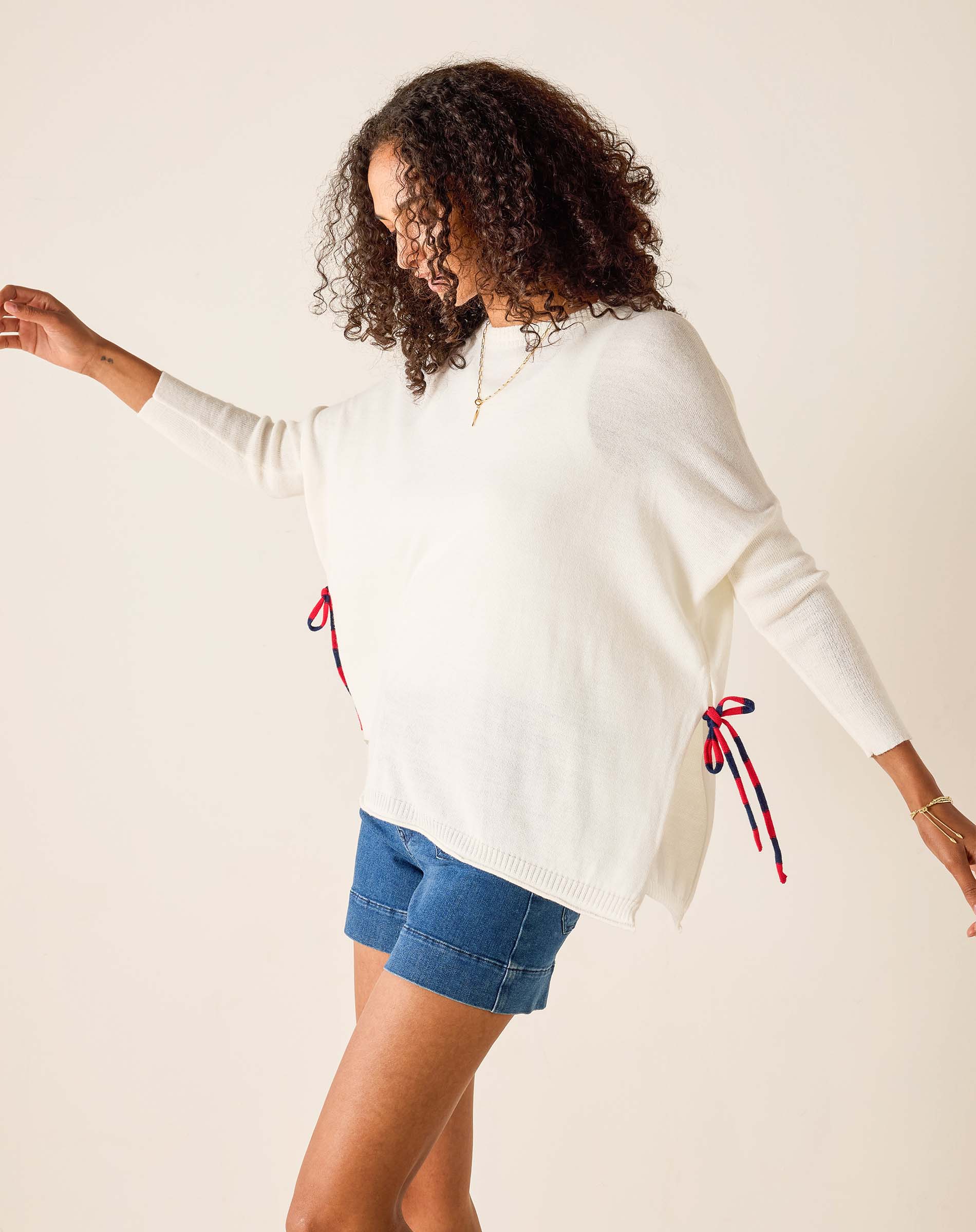 Woman wearing a white sweater with red and blue accents and denim shorts on a beige background