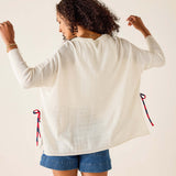 Person wearing a white cardigan with red and blue drawstrings on a plain background