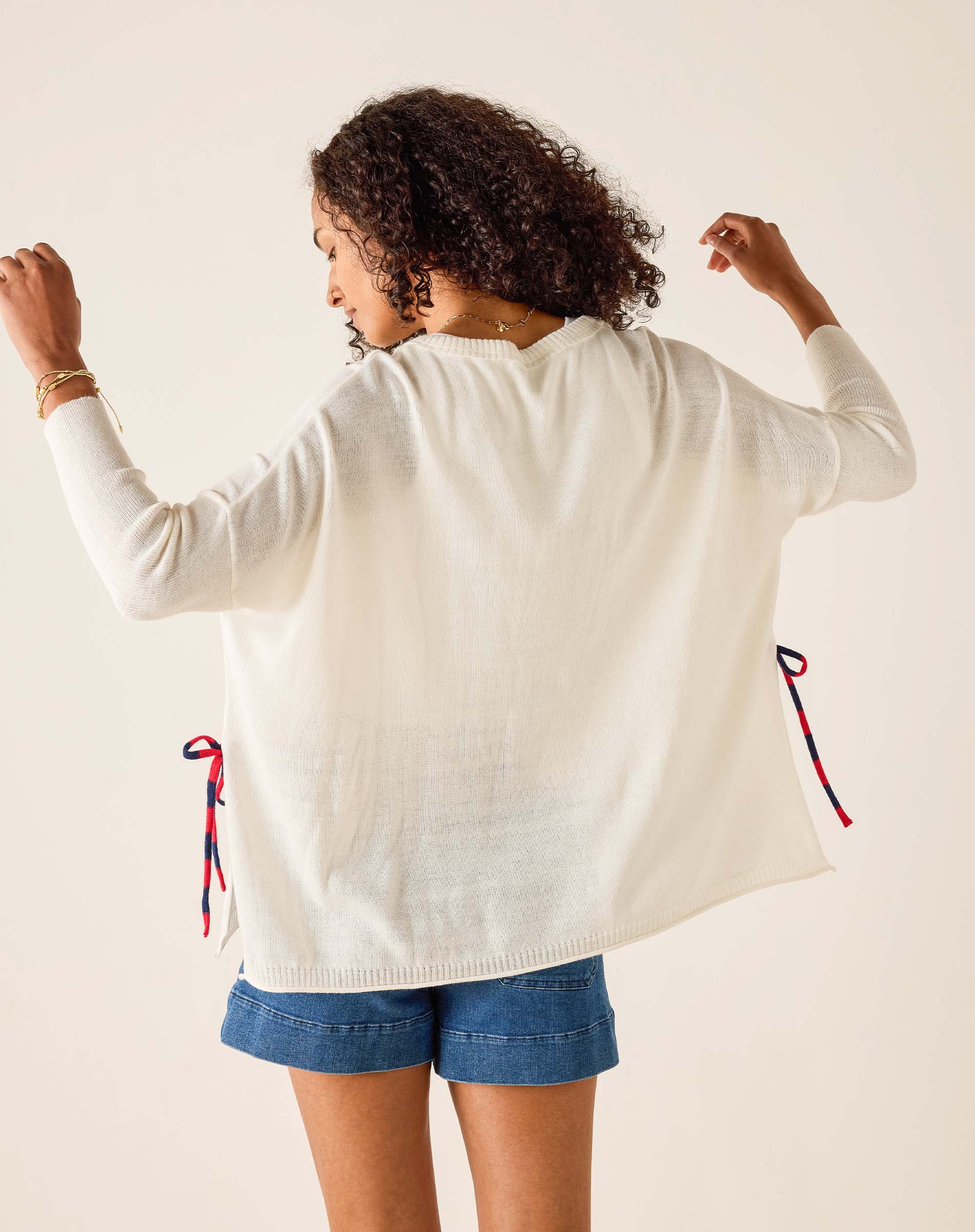Person wearing a white cardigan with red and blue drawstrings on a plain background