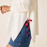 Person wearing a white sweater and blue denim skirt with red tassels on a beige background