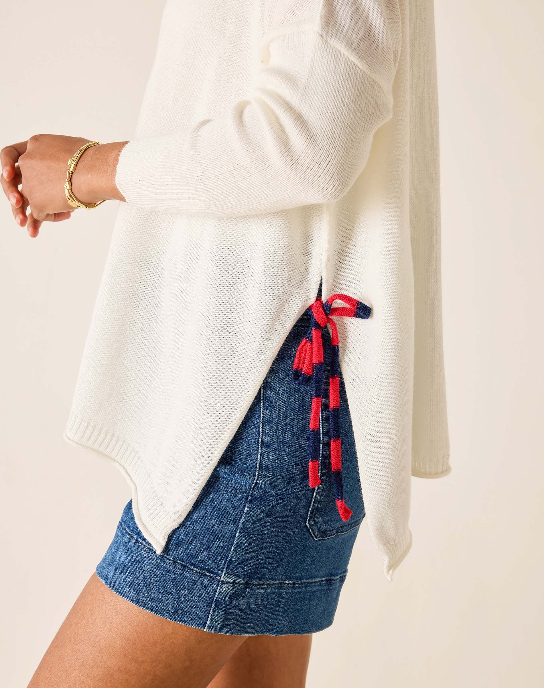 Person wearing a white sweater and blue denim skirt with red tassels on a beige background