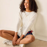 Woman sitting on the floor wearing a white sweater and blue shorts with red accents.