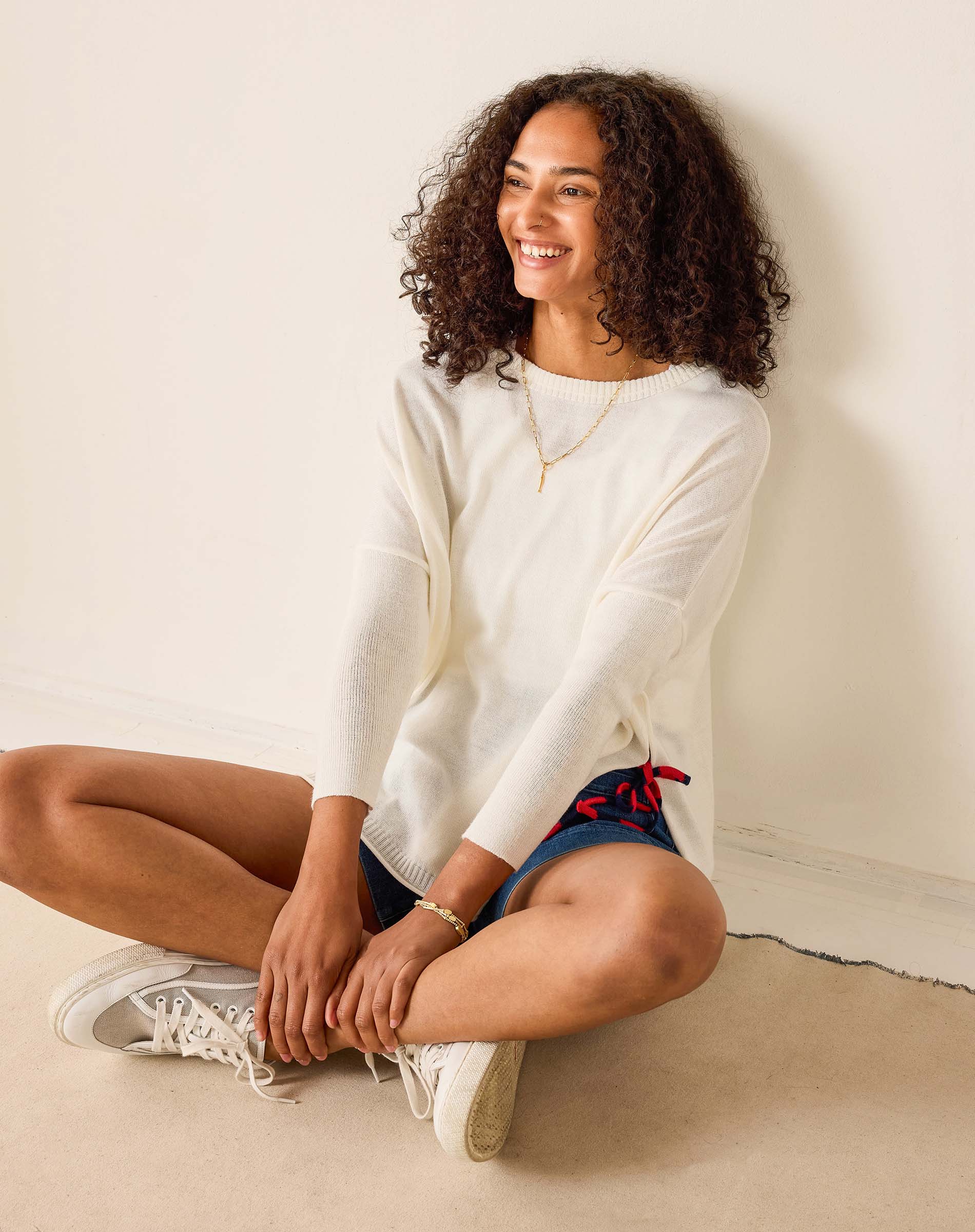 Woman sitting on the floor wearing a white sweater and blue shorts with red accents.