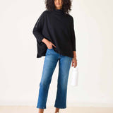 Woman wearing a black top and blue jeans against a white background