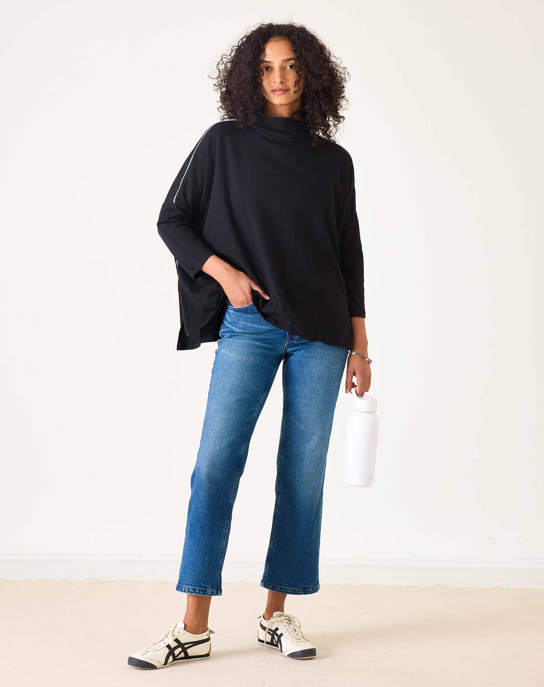 Woman wearing a black top and blue jeans against a white background